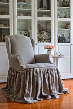 a chair with a ruffled skirt sitting in front of a china cabinet