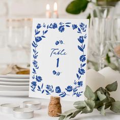 a place card with blue flowers and leaves is on a table next to some candles