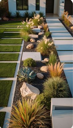 a garden with rocks, grass and plants in front of a white house at dusk