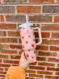 a person holding onto a pink cup with strawberries on it against a brick wall