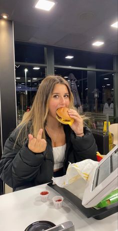 a woman sitting at a table eating a burger and giving the thumbs up sign with both hands