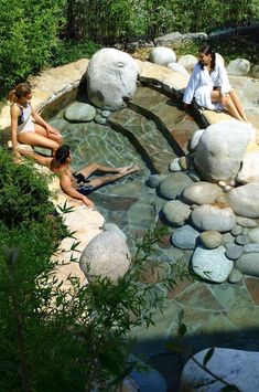 three people are sitting on rocks in the water and one person is laying down next to them