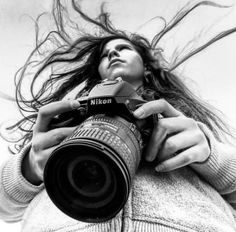 a woman holding a camera up to her face with long hair blowing in the wind