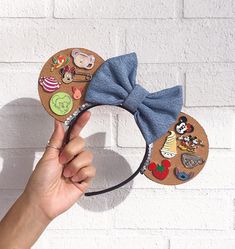 a person is holding up a mickey mouse ears headband with patches and bows on it