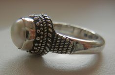 "Bali Suarti sterling silver and pearl ring. Small and beautiful, this ring has a soft iridescent white pearl, set in a raised bezel. The slightly domed pearl is encased in two rows of fine granulation pebbles and two rows of fine braiding. The sides have a striped-pebble vertical design. The back of the setting is solid and the band is thick. Beautifully made in the Balinese tradition and in excellent vintage condition. Please see detailed measurements below. > Size 5.5. *Thank you for doubl Adjustable Pearl Drop Ring, Handmade Silver Pearl Ring For Formal Occasions, Silver Pearl Ring With Cabochon, Unique Silver Pearl Ring For Anniversary, Hallmarked Sterling Silver Pearl Ring, Adjustable Pearl Drop Round Rings, Unique Sterling Silver Pearl Ring In Silver, Unique Sterling Silver Pearl Ring, Silver Rings With Pearl Drop