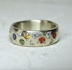 a silver ring with seven different colored stones on it's side, sitting on a white surface