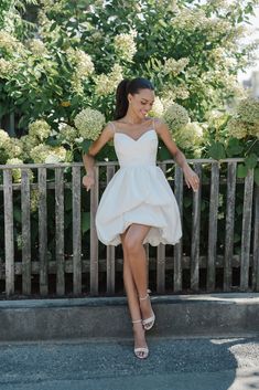 a woman in a white dress leaning against a wooden fence with her legs spread out