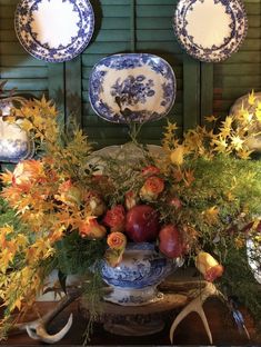 an arrangement of flowers, apples and deer antlers on display in front of green shutters