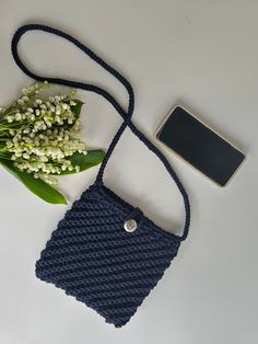 a cell phone and some flowers on a white table next to a blue knitted bag