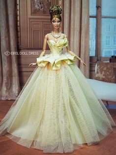 a barbie doll wearing a yellow dress and tiara in a living room with chandelier