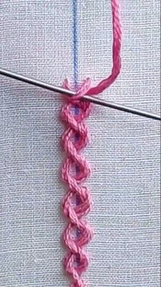 a close up of a pink crochet stitch on a piece of fabric next to a knitting needle