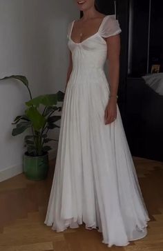 a woman in a white wedding dress standing on a wooden floor next to a potted plant