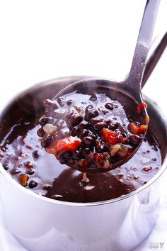 a spoon full of black beans and onions in a saucepan on a white surface