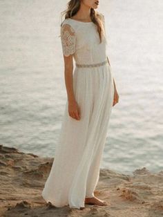 a woman standing on top of a beach next to the ocean wearing a white dress