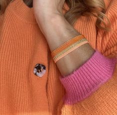 a woman in an orange sweater is talking on her cell phone and wearing a bracelet