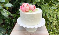 there is a white cake with pink flowers on top and greenery in the background