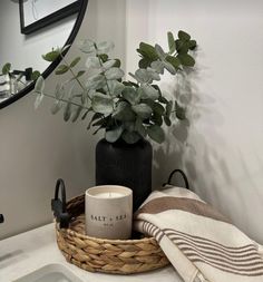 a bathroom sink with a basket and towel on it, next to a plant in a vase