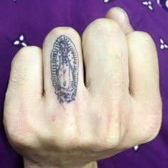 a person's hand with a small tattoo on the middle finger and an image of a virgin mary