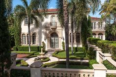 a large white house surrounded by palm trees and bushes with a fountain in the front yard