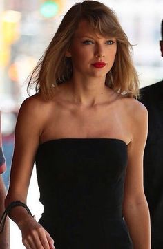 the woman is walking down the street with her hand on her hip and wearing a strapless black dress