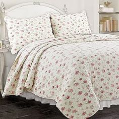 a white bed topped with pillows and a comforter covered in pink flowers on top of a wooden floor