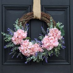 a wreath with pink flowers and greenery hangs on a black door