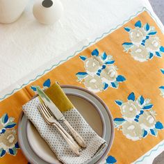 a place setting on a table with yellow and blue napkins, white plates and silverware