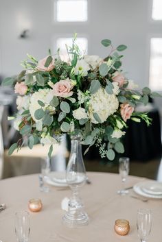 a vase filled with white flowers and greenery on top of a round dining table