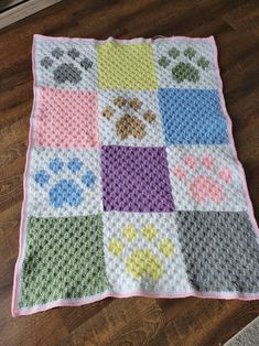 a dog themed crocheted blanket is on the floor next to a cat's paw print