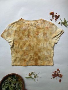 a t - shirt that has been dyed yellow and is next to some dried flowers