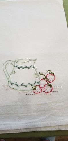 an embroidered tea towel with strawberries on the edge and a pitcher in the background