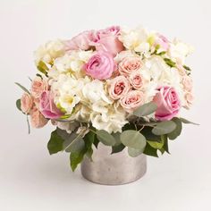 a bouquet of pink and white flowers in a silver vase on a white background with greenery