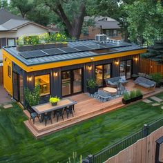 a small house with solar panels on the roof and patio area, surrounded by green grass