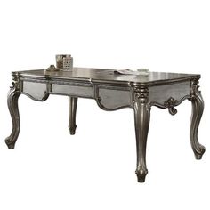 an antique style desk with silver paint and wood trimmings on the legs, in front of a white background