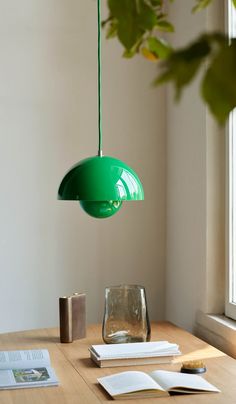 a green light hanging over a wooden table next to a book and glass vase on top of it