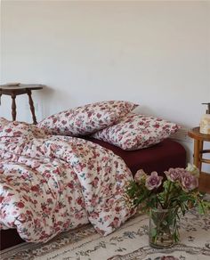 a bed with two pillows on top of it next to a vase filled with flowers