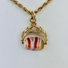 "This is a beautiful Victorian style Swivel Fob Seal / Pendant in 9K / 9ct yellow gold. The spinning fob pendant features hand carved floral gold design and a triangle shaped banded agate with vibrant white, red/orange, and yellow colors. The fob measures 0.87\" (22.3mm) high including bail without split ring and 0.76\" (19.4mm) wide at it is widest point. It is fully hallmarked for Birmingham Assay, 9ct gold, and year letter for 1977. It weighs 3.862 grams. All of our listings come in a box rea Gold Agate Hallmarked Jewelry, Classic Formal Agate Jewelry, Yellow Gold Oval Agate Jewelry, Oval Agate Yellow Gold Jewelry, Oval Yellow Gold Agate Jewelry, Antique Gold Agate Jewelry, Formal Agate Jewelry With Engraving, Formal Engraved Agate Jewelry, Vintage Gold Agate Jewelry