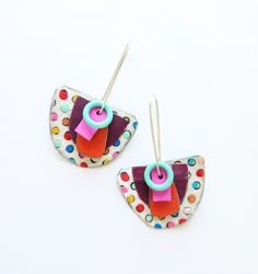 two pairs of earrings with colorful designs on them sitting on a white surface and one pair is hanging from the back