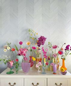 a white dresser topped with lots of vases filled with flowers next to a wall