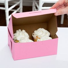 two cupcakes in a pink box on a table