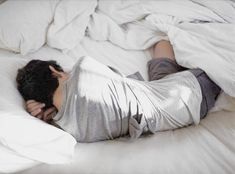 a man laying on top of a white bed covered in sheets and pillows with his head under the covers