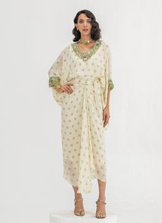 This elegant Ivory Embroidered Toga Cape Skirt Set is a timeless blend of sophistication and comfort. Crafted from soft crepe fabric, the set features a Ivory-colored, loose-fitting cape adorned with intricate floral embroidery around the neckline and cuffs. Paired with a wrap-style skirt that accentuates the waist and drapes effortlessly, it creates a flattering fit while ensuring easy movement. Ideal Indo-Western attire for home poojas, family gatherings, or festive occasions. Composition : Top and Skirt - Crepe Care: Dry Clean Only and Vacuum Storage This product can be customized for sleeves, blouse length and neckline Delivery : 4-6 weeks as the product is hand crafted. Check Size Guide or choose MySize for free customisation (All Sizes above XL can be made at 15% additional cost) For Beige Silk Dress With Traditional Drape, Elegant Georgette Dress With Embroidered Border, Traditional Off-white Dresses With Pearl Embroidery, Traditional Off White Dress With Pearl Embroidery, Cream Georgette Dresses With Pearl Embroidery, Cream Pearl Embroidery Georgette Dress, Traditional Cream Dress With Pearl Embroidery, Off White Embroidered Georgette Dress, White Embroidered Silk Kaftan