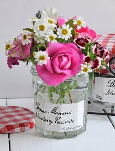 two jars filled with flowers sitting on top of a white wooden table next to a red checkered napkin