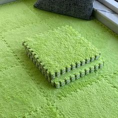 a bright green rug on the floor next to a window with a pillow and pillows