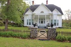 a white house with a gate in front of it and some bushes around the yard