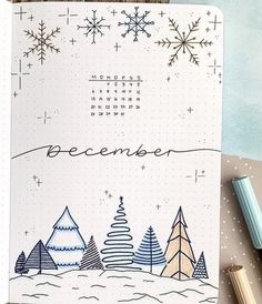 an open notebook with christmas trees and snowflakes on the cover, next to some crayon markers