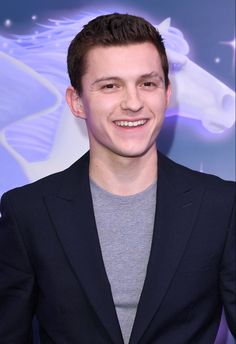 a smiling young man in a suit and grey shirt with a horse on the wall behind him