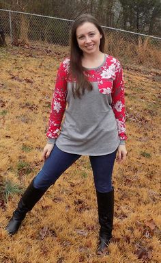 a woman standing in the middle of a field wearing boots and a shirt with flowers on it