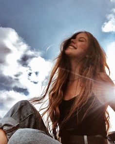 a beautiful young woman sitting on top of a skateboard under a blue cloudy sky