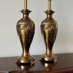 two golden vases sitting on top of a wooden table next to each other with candles in them